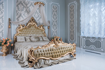 Luxury bedroom in light colors with golden furniture details. Big comfortable double royal bed in elegant classic interior