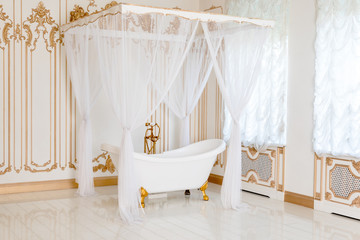 Fototapeta na wymiar Luxury bathroom in light colors with golden furniture details and canopy. Elegant classic interior.