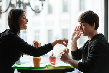 Young woman trying to eat burger of her brother
