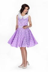 Charming girl in purple dress with polka dots turns around looking at camera on white background