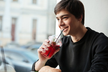 Happy young man sitting in cafe drinking juice.