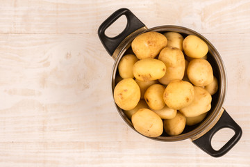 Flat lay young potatoes in the metal pot above wooden background