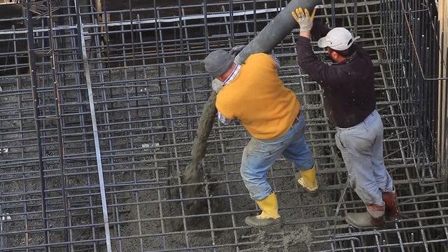 Two workers pulling the large hose of a concrete pumping machine for concreting on rebar grids at the construction site. 