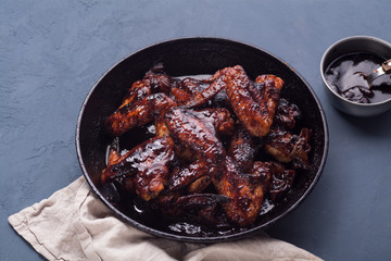 Chicken wings in thick barbecue sauce with garlic on black cast iron pan on gray rustic background.
