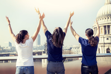 group of three young friends lift their arms to the sky on a london terrace