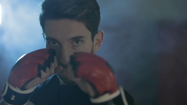 Ragazzo serio alza lo sguardo alla telecamera prima di allenarsi. Sfondo con luce blu e fumo bianco.