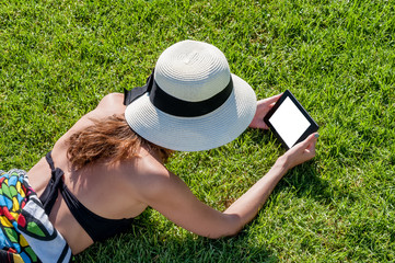 Girl lying on grass reading electronic book