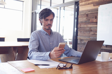 Mid-adult white man at desk in an office using smartphone