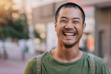 Asian man laughing while standing on a city street