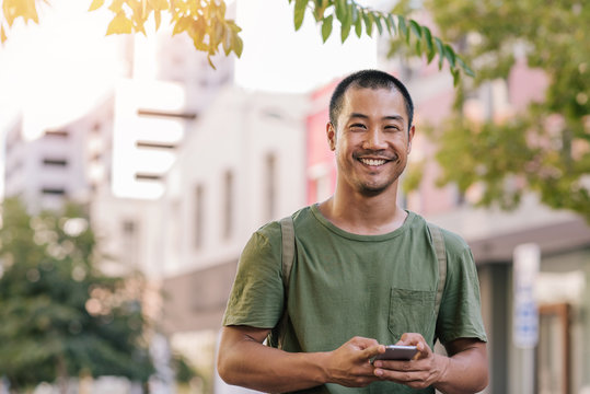 Young Asian Man Sending A Text On His Cellphone Outside