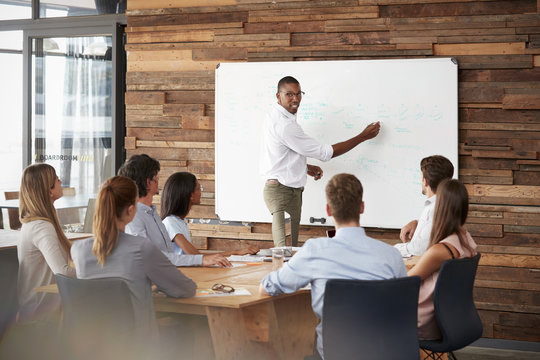 Young black man stands at whiteboard addressing team at meeting