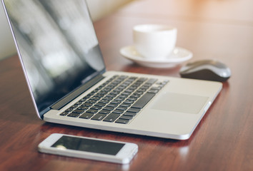 laptop, cell phone, coffee cup on wood table background in office.