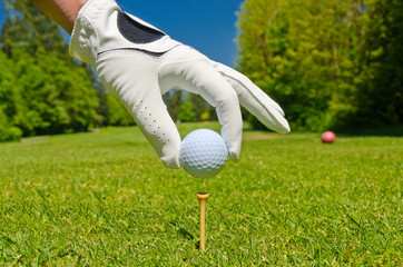 hand placing golf ball on tee over beautiful golf course with blue sky