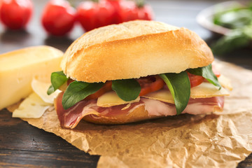 One delicious sandwich on a brown paper bag with some tomatoes in the background