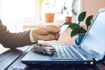Man in the suit working in the office at a laptop, holding a car paying with a credit card