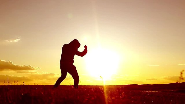 Silhouette of man exercising thai boxing. Silhouette of martial arts man training boxing on the beach over beautiful sunset background. Training karate or boxing on grass field at sunset.