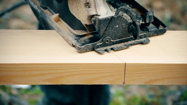 Cutting a wooden plank with a portable circular hand saw. The sawdust flies around.