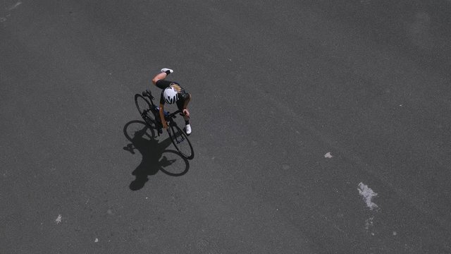 Young female athlete on her professional aero carbon road bike strolls through the street wears her lycra outfit and lightweight helmet, stops to check cycling computer garmin for directions,top view