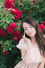 Красивая девушка с темными длинными волосами рядом с красными розами в саду