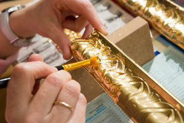 female hand painting with a brush baguette for ceiling in gold color