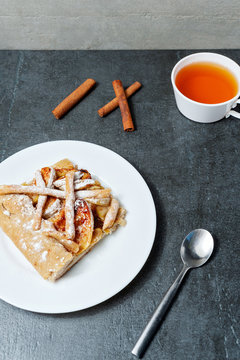 Homemade apple pie and tea and cinnamone sticks on dark background.