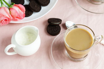 Tea with milk in a glass cup and cookies on a pink background 