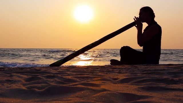 Didgeridoo playing. Male Silhouette with Didgeridu near Sea.