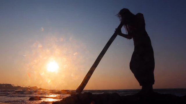 Didgeridoo playing. Male Silhouette with Didgeridu near Sea.