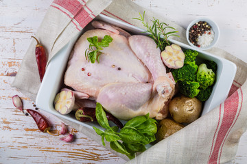 Raw whole chicken with herbs and spices on rustic wood background