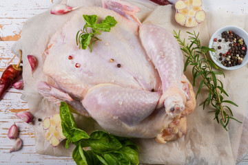 Raw whole chicken with herbs and spices on rustic wood background