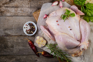 Raw whole chicken with herbs and spices on rustic wood background