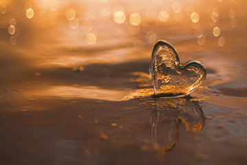 clear glass heart on  sand beach with sunrise sun light