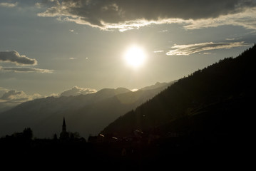 Mountain landscape during sunset, backlit mountain profile, a small church and mountain village and plants, alps, switzerland