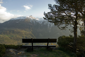 Panorama: Snowy mountains photographed in spring during sunset, in the foreground a wooden bench, Alps, Switzerland