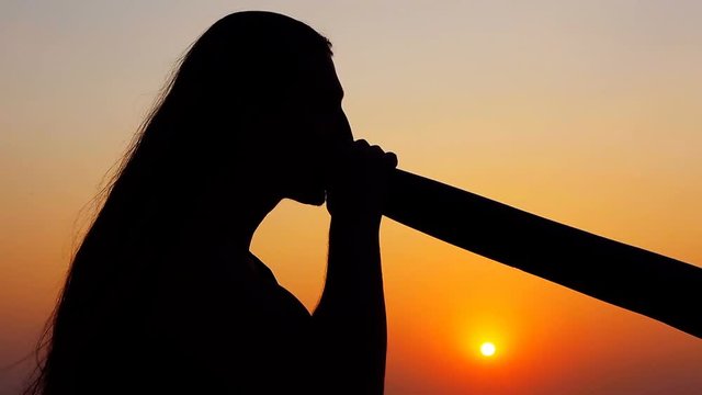Didgeridoo playing. Male Silhouette with Didgeridu near Sea.