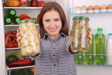 Young girl hold canned champignons and cucumbers on the refrigerator background
