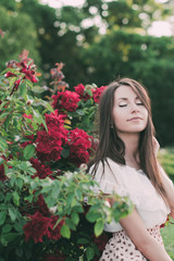 Портрет красивой девушки с длинными темными волосами рядом с красными розами в саду 