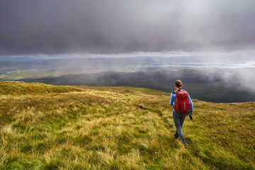 A hiker and their dog descending Macleod's Table (North) towards Glen Osdale on the Isle of Skye,...