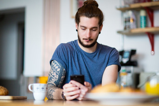 Young adult male having morning coffee and checking smartphone