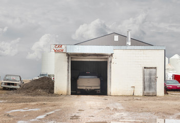 horizontal image of a very old car wash building with a truck being washed inside on a very rainy day.