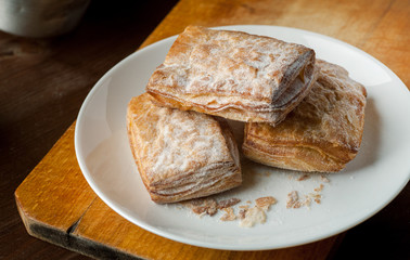 Puff pastry cookies in a white plate on a wooden cutting board