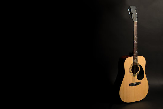 Acoustic guitar on a black background on the right side of the frame, half-turn. Stringed instrument. Horizontal frame.