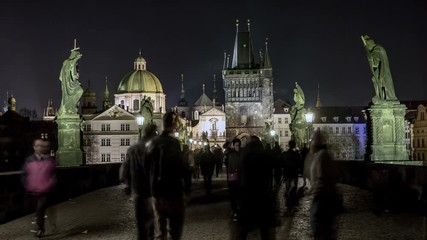 Impressive view on the Charles bridge in Prague with old and arty sculptures, lit lanterns, streaming back and forth people in the evening twilights, in early spring, being taken as a timelapse shot