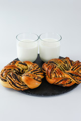 Baked pastry with poppy seeds on black plate with glass of milk with white background