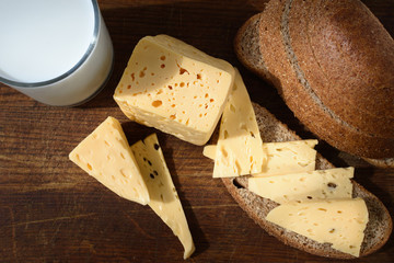 Cheese is cut into pieces on a wooden board, bread and a glass of milk