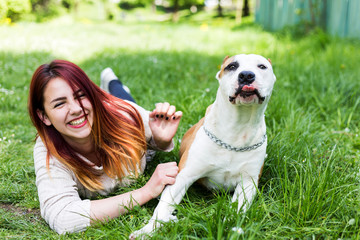 Beautiful young girl hugging her dog and lying on the green grass in the park.