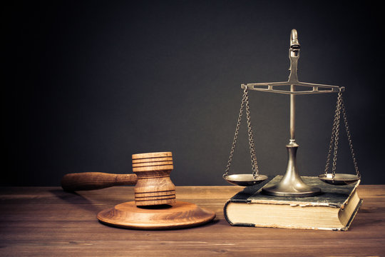 Law scales, wooden gavel and book on table front dark background. Symbol of justice. Retro style filtered photo