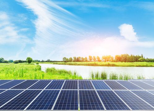 Solar panels and pond on green grass with blue sky