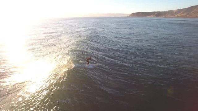 Aerial view of standup paddle surfing (SUP) a wave at sunset