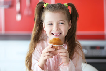 Cute little girl with tasty muffin on blurred background
